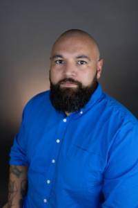 The head and torso of male-appearing person with a beard and a blue shirt