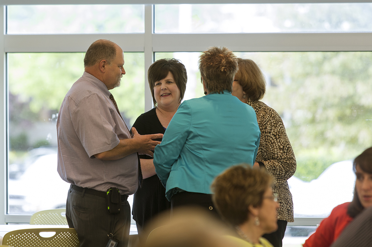 A seated faculty member holds an ipad and motions to students