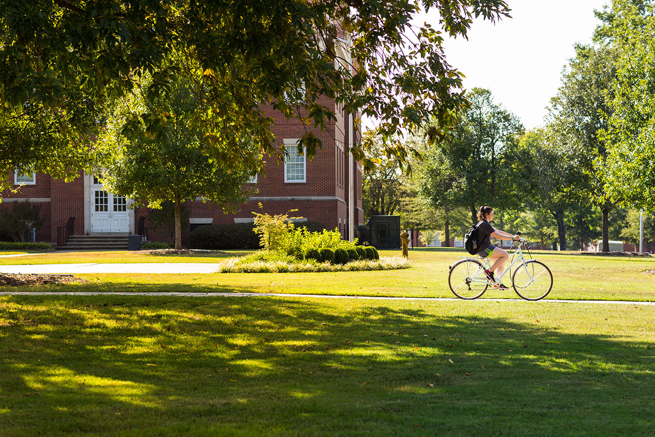 a photo of a student riding a bicycle on campus in the sunshine