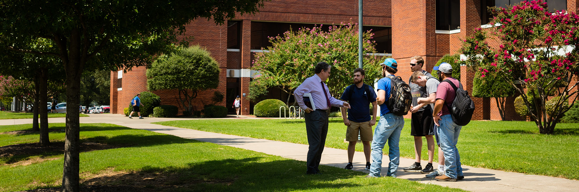 a group of students speak with a faculty member outside of corley hall